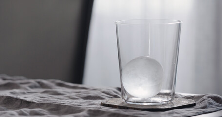 clear ice ball in tumbler glass on walnut table