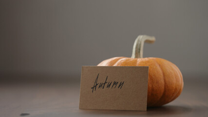 autumn card next to small orange pumpkin on walnut table
