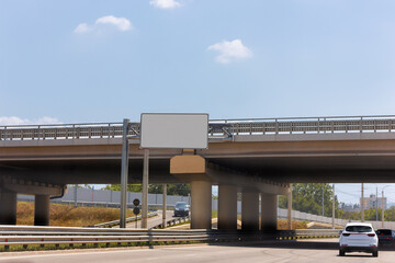 Road junction, overpass, cars, road signage. Bumpers, and the railing of the overpass. Photo.
