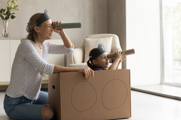 Joyful bonding young mother and little cute kid daughter looking in spyglasses, playing interesting pirates game in modern living room. Happy family having fun, entertaining together at home.