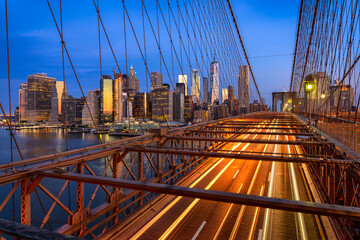 Manhattan and Brooklyn Bridge with light tails of traffic and background of building skyscraper at blue hour, New York City