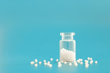 Close-up image of homeopathic globules in glass bottle on blue background. Homeopathy pharmacy,...