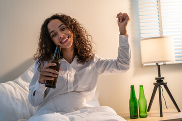 Drunk Latino woman hold beer bottle, feel hangover and dancing on bed.