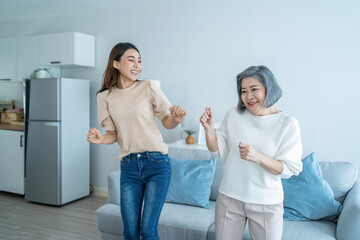 Asian funny senior old mom and daughter dance together in living room. 