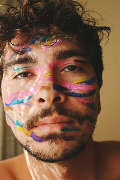 closeup portrait of  calm & happy queer young mans face expression with colorful facepaint