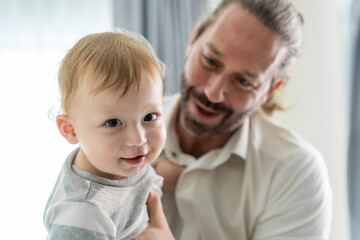 Caucasian loving father holding baby boy child in house living room.