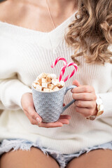Fototapeta na wymiar Girl in knitted wool sweater is holding a mug with hot chocolate with marshmallow.