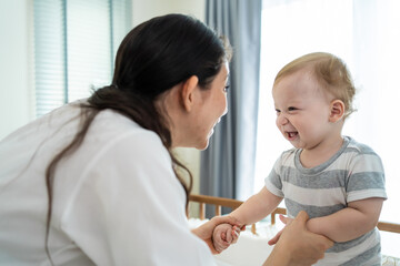 Fototapeta premium Caucasian mother play with cute baby boy child on infant bed at home.