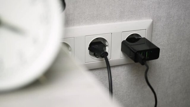 Hand plug black mobile charger adapter into the wall power socket close-up view