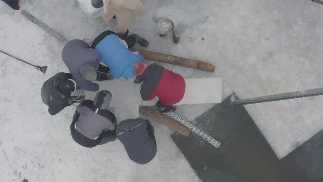 Preparing font on pond in form of cross for Epiphany bathing on feast of Baptism of Lord. Top view of group of men pulls out huge ice cross from hole with water