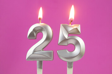 Burning silver birthday candles on pink background, number 25