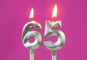 Burning silver birthday candles on pink background, number 65