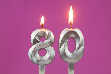 Burning silver birthday candles on pink background, number 80