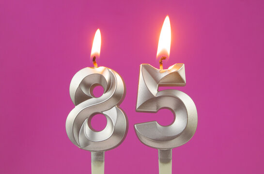 Burning silver birthday candles on pink background, number 85