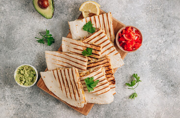 Grilled quesadillas on wooden board and with salsa and guacamole on stone background. Mexican cuisine concept Quesadilla wrap with chicken and corn.