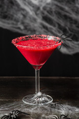 Top view of glass with red halloween cocktail with spider, on wooden table, black background with spider web, vertical
