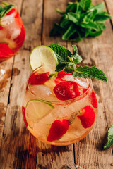 Fresh lemonade with green tea, lime, mint and strawberry on wooden background. Cold summer drink. Two glasses with berry ice tea. Selective focus.