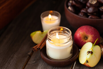 Obraz na płótnie Canvas Composition with aromatic candles, apple, cinnamon, chestnut. Cozy home atmosphere, aromatherapy. Dark wooden background