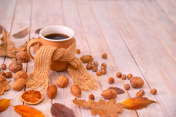 Autumn, autumn leaves, a cup of hot coffee wrapped in a warm scarf on a wooden table background, copy space. Seasonal, morning coffee, relaxing Sunday and the concept of warmth and comfort. 
