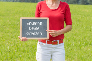 Eine Frau mit einer Tafel auf der Erkenne Deine Grenzen steht