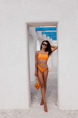 beautiful woman with dark hair in elegant swimming suit posing in white hotel of Santorini