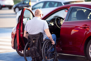 Person with a physical disability getting in red car fom wheelchair