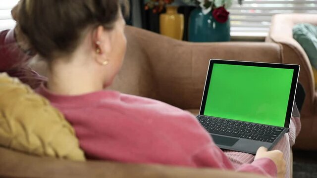 Young woman, girl relaxing at home on the couch and using laptop computer. Back view of girl watching movie on laptop at home. Green screen Over the shoulder shot of young woman working on modern lapt
