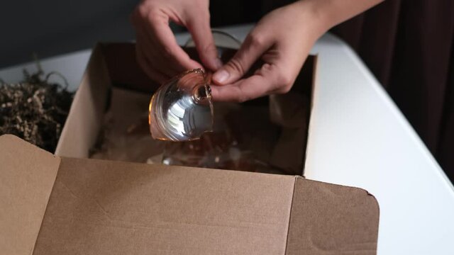 woman opens a delivery box from a store and discovers a broken glass. An improperly packed item crashed on delivery
