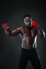 Athletic boxer during boxing training. Fitness african american muscular model over black background. Strength, fighting and motion project.