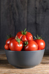 Ripe raw red tomatoes in a bowl on rustic wooden table. Side view