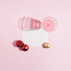 Visual New Year and Christmas decoration idea with a drinking glass, red and gold baubles. White copy space card, vivid pink background. Minimal flat lay composition. 2021 and 2022 holiday season.