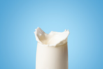 Milk splash on the edge of clear glass isolated on blue background, empty space for text and...