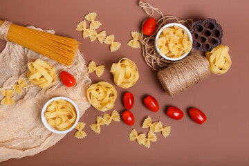 Dry italian pasta and cherry tomatoes from above in rustic style on brown background. Pasta is the traditional italian food Spaghetti, fettuccine, farfalle, cherry tomatoes, egg, flour in rustic style