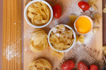 Yummy italian pasta and cherry tomatoes in rustic style on brown background. Traditional italian cuisine top view. Pasta is the traditional italian food. Spaghetti, fettuccine, farfalle flat lay view.