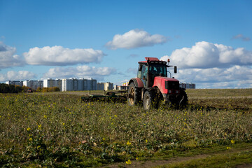 Fototapeta premium A farmer in a tractor, agricultural machinery, prepares the land with a cultivator. A modern red tractor in a field. Plowing a heavy tractor while cultivating agricultural work in a field with a plow.