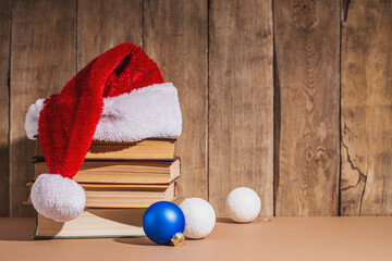 Obraz na płótnie Canvas Stack of books, Christmas tree decorations and Santa Claus hat on wooden background