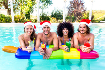merry christmas! happy diverse group of friends portrait wearing xmas santa hat having drinks in swimming pool party celebrating winter warm festivities outdoor. family time and summer holiday concept
