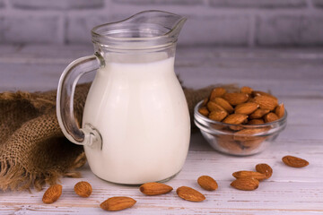 Healthy almond milk in a jug and almonds on a white wooden background.