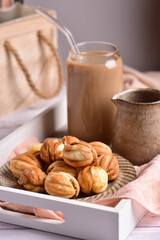 Nuts with condensed milk on a tray, behind a glass of coffee with milk.