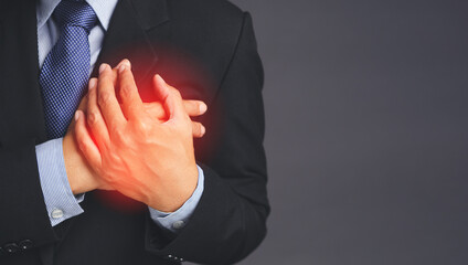 The businessman in the suit has sore left chest pain while standing on gray background in the studio. Close-up photo. Medical and health care concept