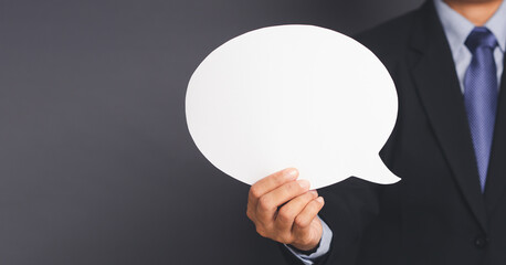 Business and speech bubble concept. Businessman in suit hand holding an empty speech bubble paper while standing on gray background in the studio. Space for text. Close-up photo