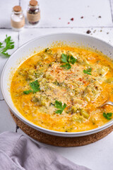A plate of cheese soup, with parsley, on a white stone tile, next to a gray napkin, side view.
