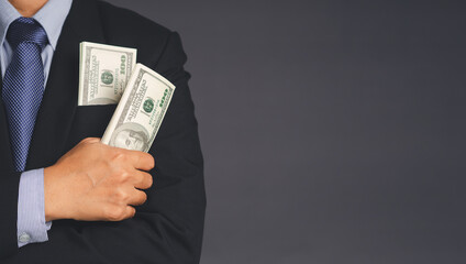 Businessman wearing a suit with US dollar banknotes in a suit pocket and holding of dollar banknotes while standing with a gray background with space for text. Business and finance concept