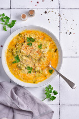 A plate of cheese soup, with parsley, on a white stone tile, next to a gray napkin, top view.