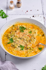 A plate of cheese soup, with parsley, on a white stone tile, next to a gray napkin, side view.
