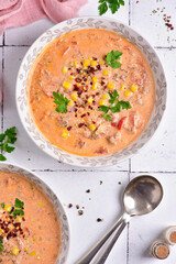 Tomato soup with parsley and corn, on a white stone tile, top view.