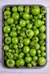 Green tomatoes of different sizes on a tray, top view.