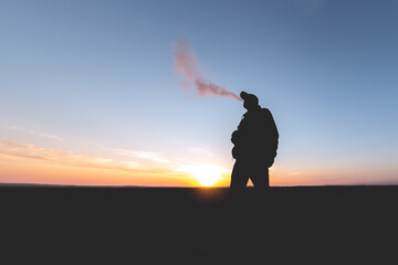 The man smoke an electronic cigarette on the sunset backround