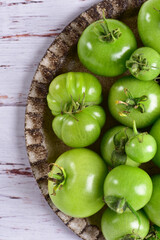 Green tomatoes on a brown plate, on a white wooden table, top view, close-up.
