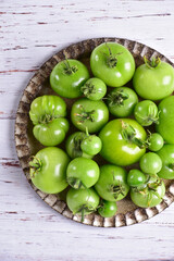 Green tomatoes on a brown plate, on a white wooden table, top view, close-up.